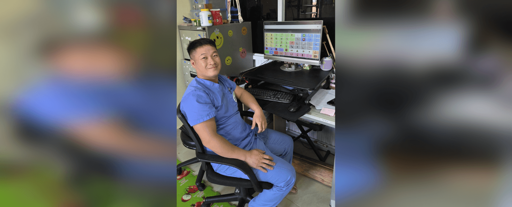 Kongmeng, a clinician wearing scrubs, sitting in front of a computer showing a translated version of the Quick Core 60 vocabulary